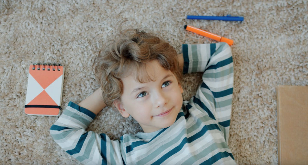 Child lying on floor with arms behind his back being looked after by a Residential Childcare Worker